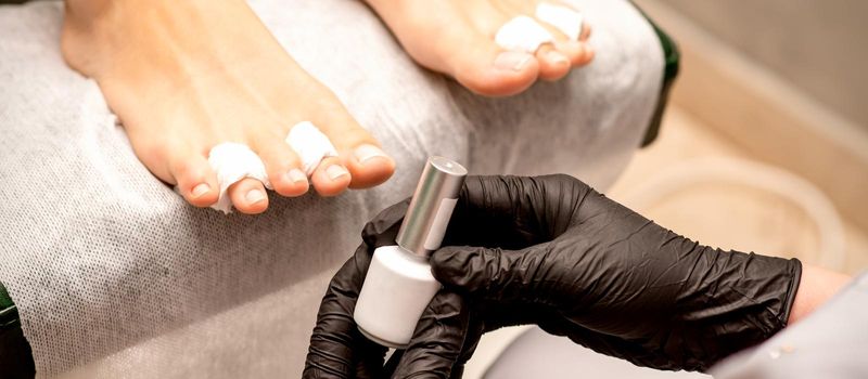 White nail polish in the hands of a manicurist while painting nails on a female feet, closeup