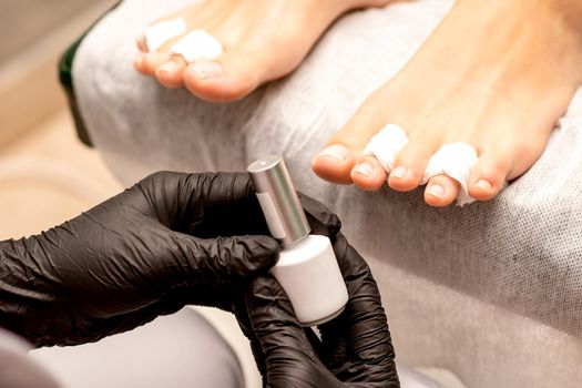 White nail polish in the hands of a manicurist while painting nails on a female feet, closeup