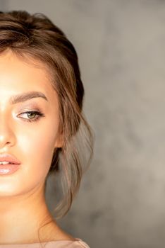 The fashionable young woman. Portrait of the beautiful female model with long hair and makeup. Beauty young caucasian woman with a brown curly hairstyle on the background of a gray wall