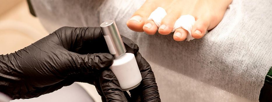 White nail polish in the hands of a manicurist while painting nails on a female feet, closeup