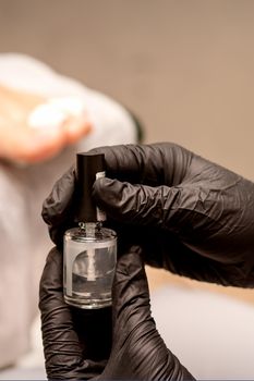 Transparent nail polish in the hands of a manicure master while painting nails on a female feet