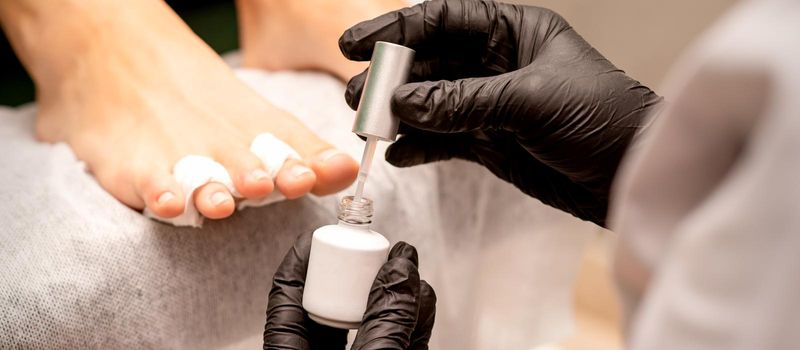 White nail polish in the hands of a manicurist while painting nails on a female feet, closeup