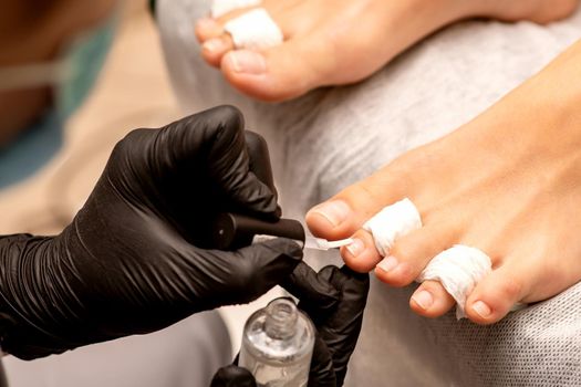 Manicure master painting nails on a female foot with transparent nail polish in a beauty salon, close up