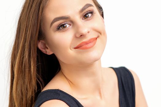 Portrait of a beautiful young caucasian smiling brunette woman with long straight hair standing and looking at the camera on white background