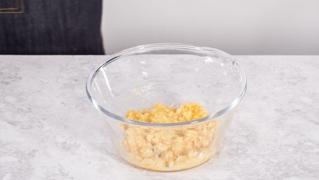 Step by step. Smashing riped bananas in a glass mixing bowl to prepare coconut banana pancakes.