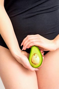 Healthy nutrition and pregnancy concept. Young woman holding one half of an avocado fruit close to her belly over a white background