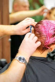 Haircut of dyed short pink wet hair of young caucasian woman by a male hairdresser in a barbershop