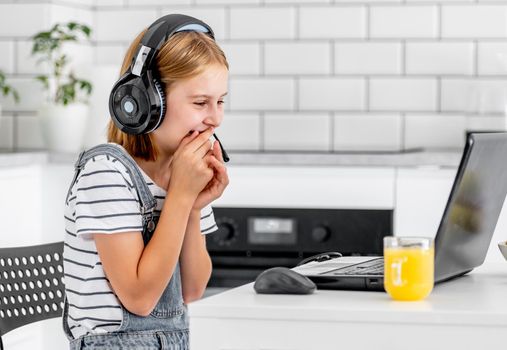 Preteen girl wearing headphones study with laptop. during online lesson at home at pandemic coronavirus. Child pupil smiling making video call with orange juice on table
