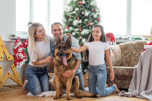 smiling family and daughter with dog sitting near christmas tree with gifts.