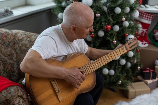 Happy people family concept - Old senior man enjoying the guitar on the sofa in the house at christmas.