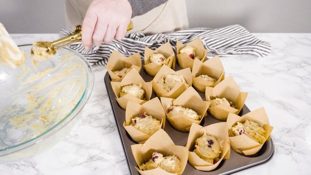 Step by step. Scooping dough into tulip muffin liners with mixture scoop to bake cranberry muffins.