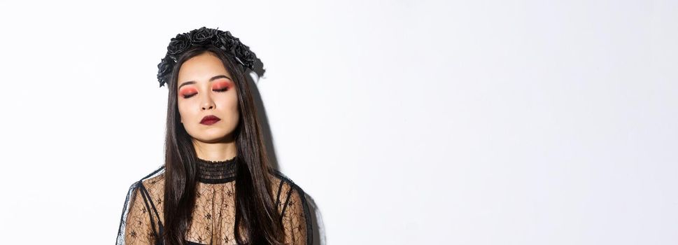 Close-up of bored asian woman sleeping while standing over white background in witch costume.