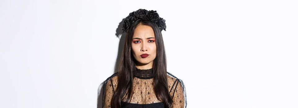 Close-up of disappointed grimacing girl in witch costume looking displeased, frowning upset, standing over white background.