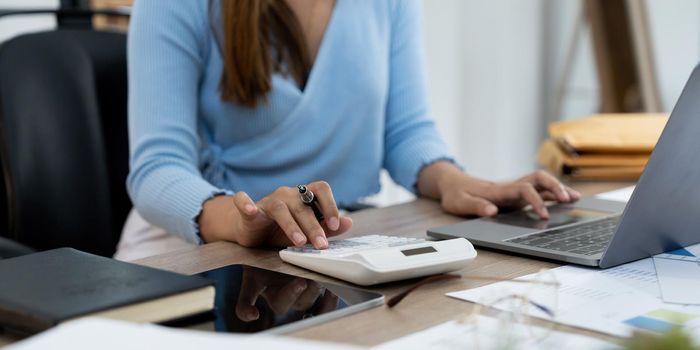 Woman hand holding pen and using calculator with doing finance on desk at home office.