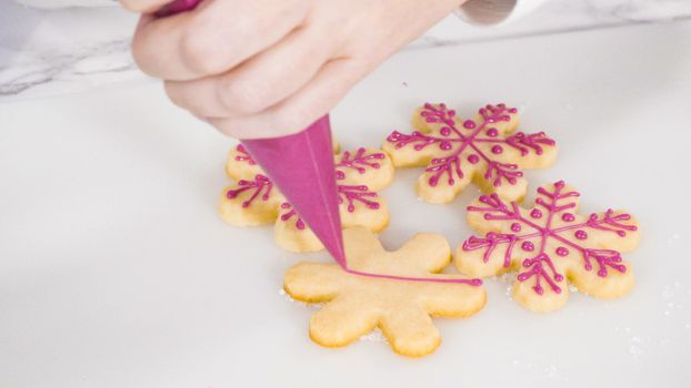 Stp by step. Icing snowflake shaped sugar cookies with pink royal icing.
