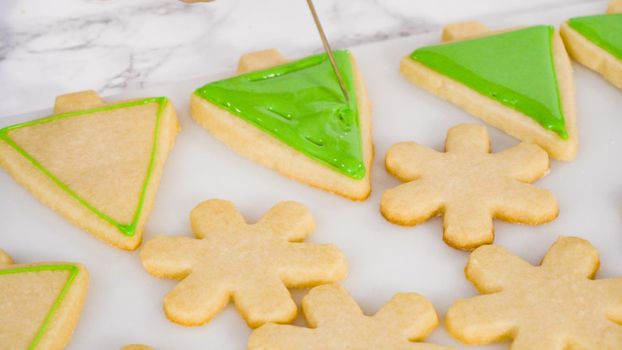 Stp by step. Icing Christmas tree-shaped sugar cookies with green royal icing.
