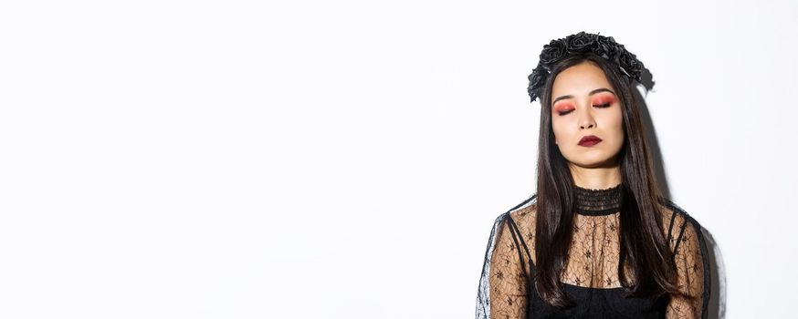 Close-up of bored asian woman sleeping while standing over white background in witch costume.