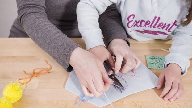 Little girl learning how to sew with her mother at the craft table.