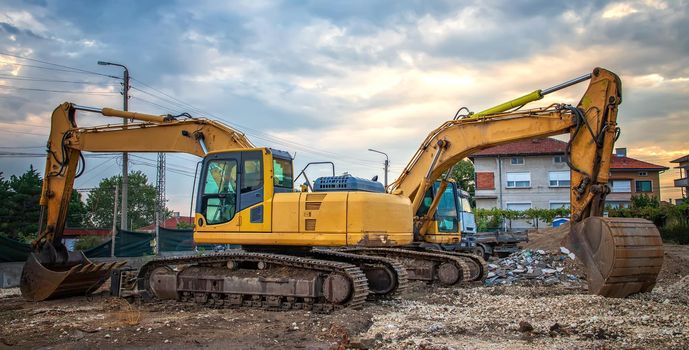 Two stopped yellow excavators at the stunning sunset. Banner view