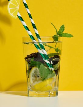 Transparent glass with lemonade, mint leaves, lemon slices and blackberries in the middle