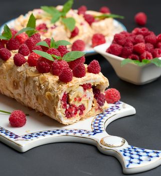 Baked meringue roll with cream and fresh red raspberry on a black wooden board, delicious dessert	