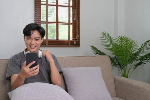 Excited young asian man hold phone chatting in dating app feel happy sit on sofa at home, Close up joyful male reading good news on phone. Surprised lady celebrating victory on phone.