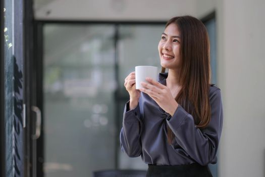 Confident Asian businesswoman standing with her arms crossed holding a coffee cup, smiling and looking at the camera..