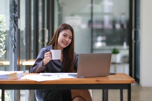 Asian Businesswoman Using laptop computer and working at office with calculator document on desk, doing planning analyzing the financial report, business plan investment, finance analysis concept..