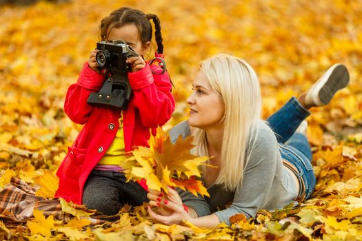 mother and daughter lying on the leaves at the autumn park