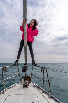 Woman standing on the nose of the yacht at a sunny summer day, breeze developing hair, beautiful sea on background.