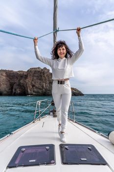 Woman standing on the nose of the yacht at a sunny summer day, breeze developing hair, beautiful sea on background.