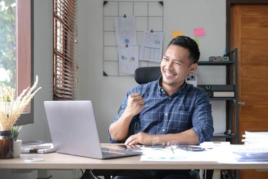 Young Asian man excited by good news celebrate success or happy pose with laptop..