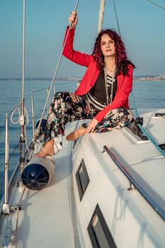 A woman sits on the bow of a yacht on a sunny summer day, the breeze develops her hair, a beautiful sea is in the background.