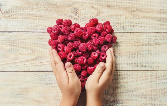 Raspberries are in the hands of a child in the form of a heart.