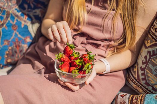 Portrait of gorgeous woman wearing beautiful dress sitting in a patio and eating strawberry.