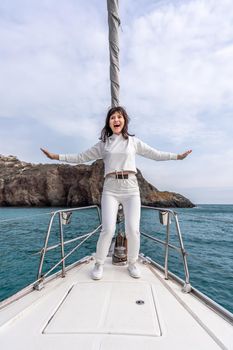 Woman standing on the nose of the yacht at a sunny summer day, breeze developing hair, beautiful sea on background.