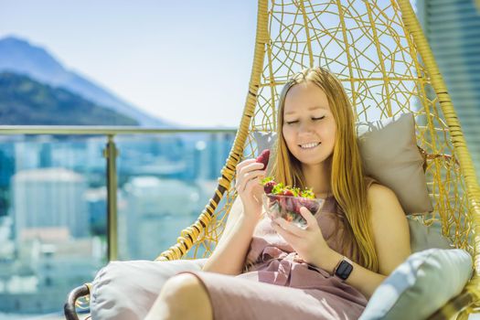 Portrait of gorgeous woman wearing beautiful dress sitting in a patio and eating strawberry.