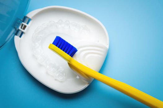 a white special box container for invisible plastic braces, aligners, with a bright yellow toothbrush lie on a blue background. nobody.