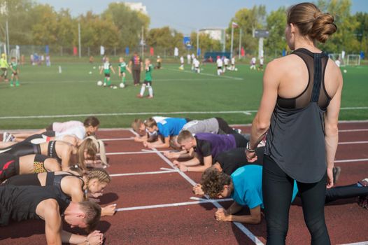 Female coach and group of children conducts a training session at the stadium. School gym trainings or athletics