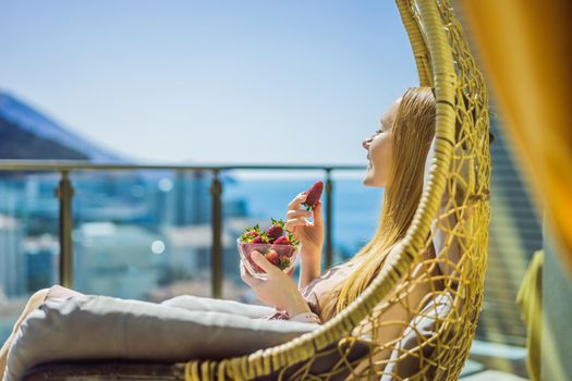 Portrait of gorgeous woman wearing beautiful dress sitting in a patio and eating strawberry.
