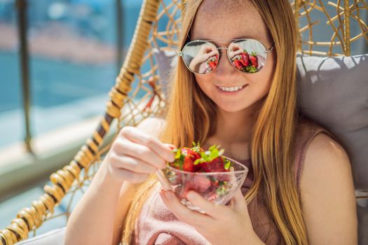 Portrait of gorgeous woman wearing beautiful dress sitting in a patio and eating strawberry.