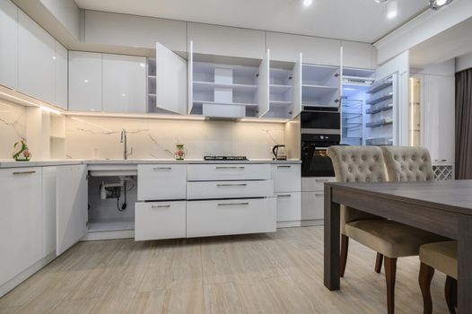 White modern new well designed white kitchen interior after renovation in studio apartment, some drawers and doors are open