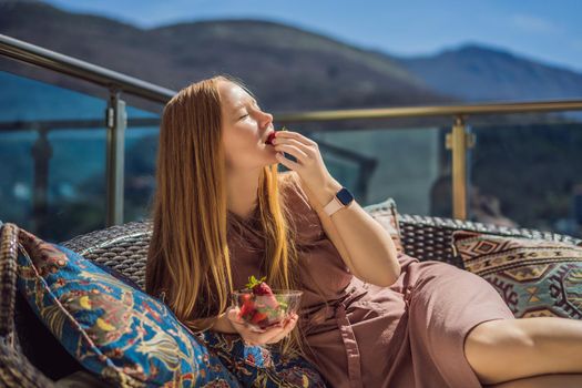 Portrait of gorgeous woman wearing beautiful dress sitting in a patio and eating strawberry.