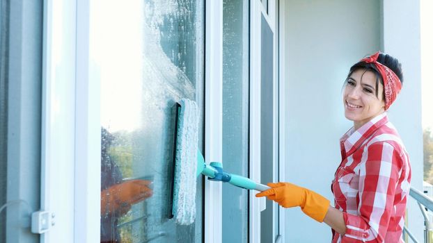 smiling Caucasian Beautiful woman, housewife or Cheerful female worker of cleaning service, in gloves, Cleaning, washing Windows by special mop, enjoying her work. Cleaning lady. High quality photo