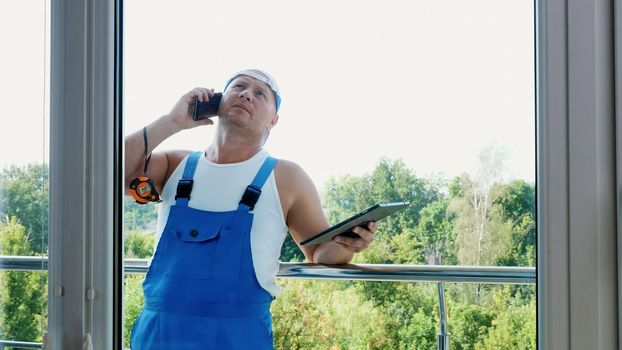attractive Construction worker is discussing something on the phone, makes measurements of windows, makes notes in tablet. service man , builder examines the object. High quality photo