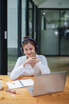 Portrait of a beautiful woman using a computer, earphone and notebook during a video conference