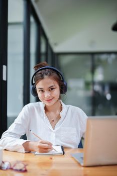 Portrait of a beautiful woman using a computer, earphone and notebook during a video conference