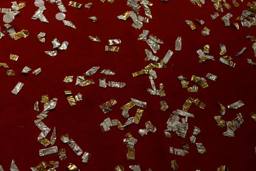Golden falling confetti on red glitter background. Christmas, festive, party or holiday background. Flat-lay, top view.