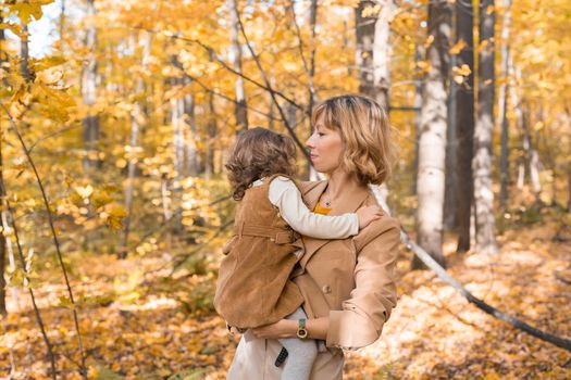 Mother with child in her arms against background of autumn nature. Family and season concept