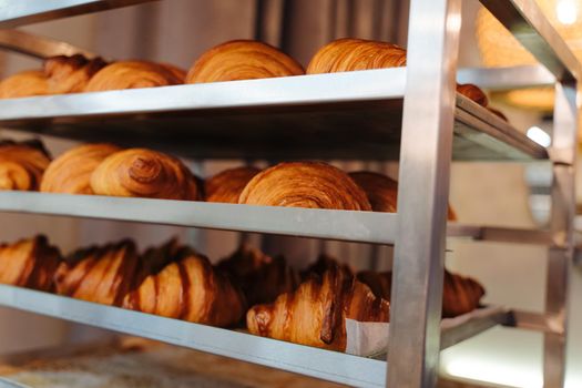 Production of delicious buns. Family bakery. Hot croissants on a metal tray. Fresh bakery. Rack with baked croissants.